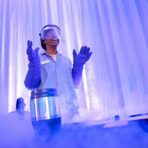 A young girl wears a lab coat, rubber gloves and safety glasses to participate in a science experiment.
