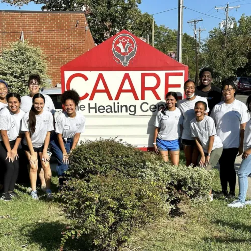 Students standing in front of the CAARE Healing Center Sign on a sunny day