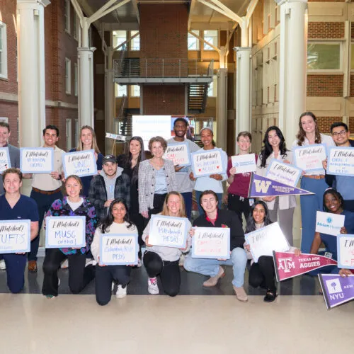 New students in the DENT Program celebrating with signs in front of them displaying what program they match with.